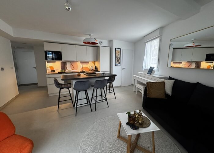 Photo de la cuisine et de l'entrée. a droite le canapé noir ou une personne peu dormir